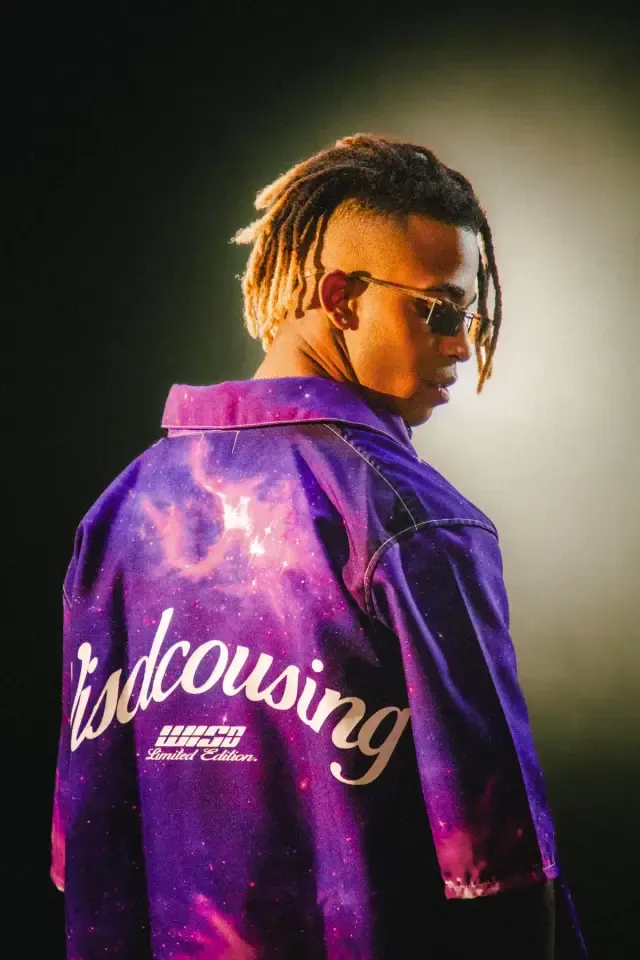 Artista visto de espaldas con una chaqueta morada de estampado galáctico y gafas de sol