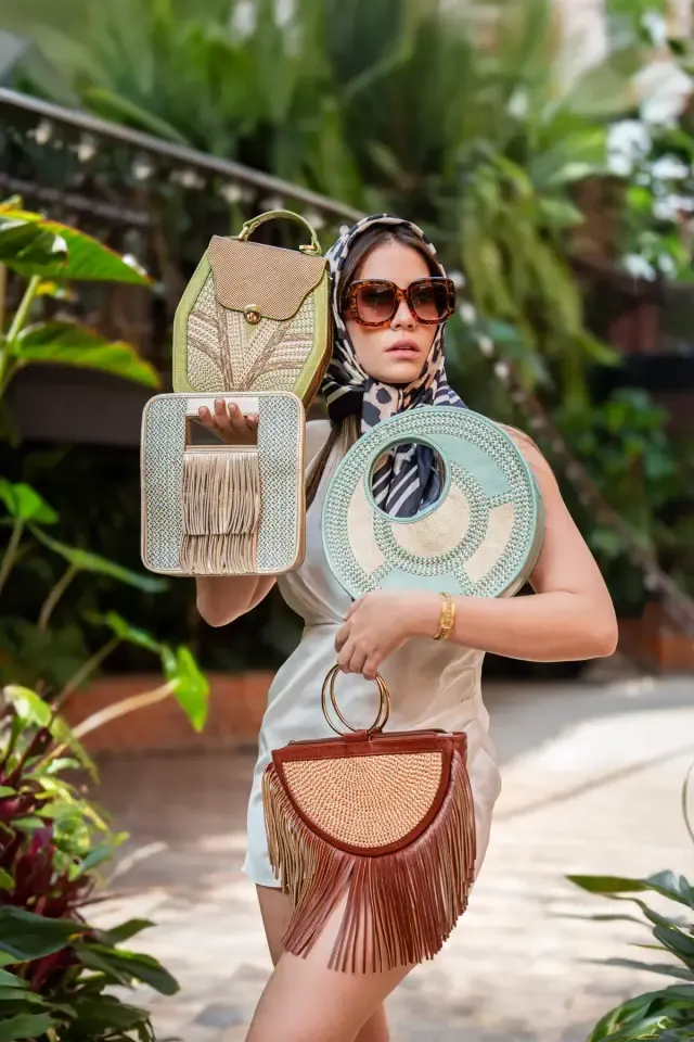 Mujer con bolsos artesanales tejidos de colores en un jardín tropical